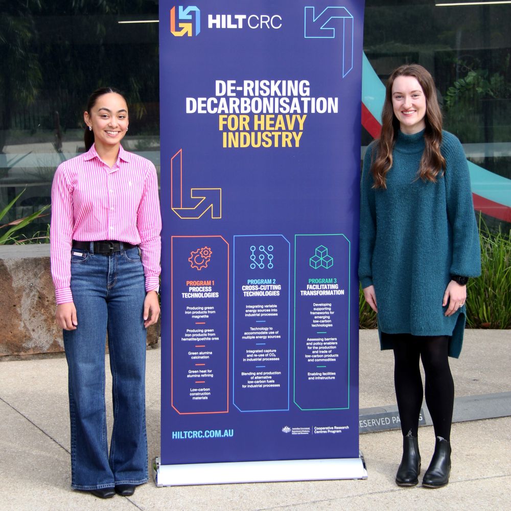 Two female engineering students, who are recipients of the 2026 HILT CRC–Adelaide University Undergraduate Scholarships, stand oitside next to a HILT CRC banner.